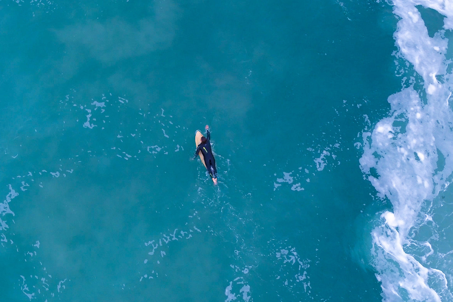 プロのアラン・ストークスが木製サーフボードで波を待つ瞬間。透明な海とボードの天然木が織りなす、静かで美しい情景。