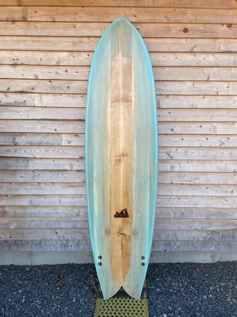 Grain Surfboardsの7'4" Frigateモデル(ボトムビュー)。ブルーティントとウッドの調和が美しいミッドレングス・フィッシュ。