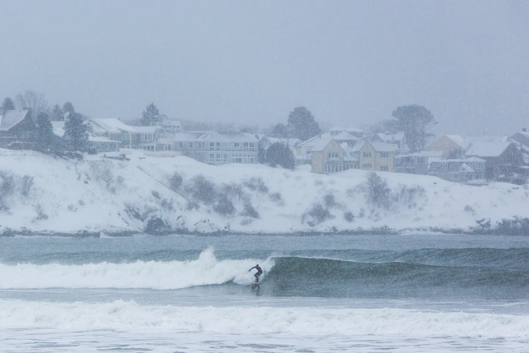 冬の絶景。白銀の景色と力強い波が織りなす中で、GRAINボードを操るサーファーの姿。