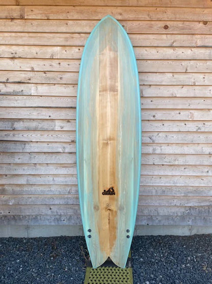 Grain Surfboardsの7'4" Frigateモデル（ボトムビュー）。ブルーティントとウッドの調和が美しいミッドレングス・フィッシュ。
