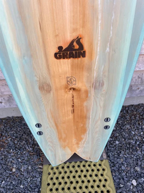 Grain Surfboardsロゴが刻まれた7'4" Frigateモデルのテール部分。クラフトマンシップと素材の温もりが伝わるディテール。