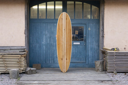 次のオーナーを待つかのような、堂々とした佇まいの中空構造（ホロー）の木製サーフボード（天然木）。クラシックなロングボードの風格と、現代的な技術が融合した大人のサーフスタイル。