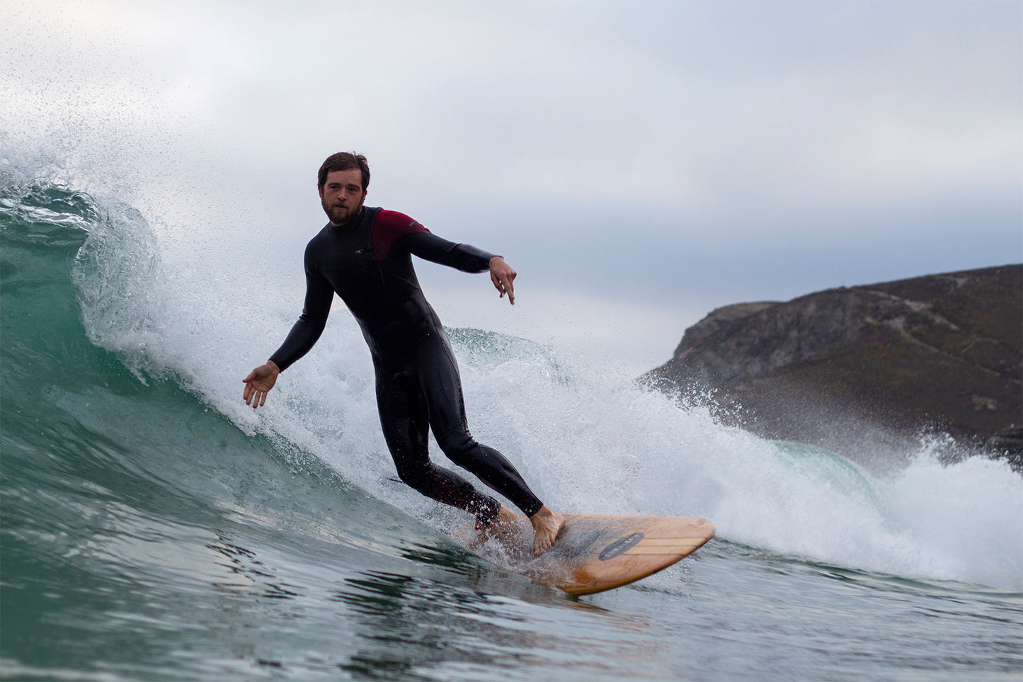 迫り来る波の飛沫と、濡れて輝きを増した中空構造（ホロー）の木製サーフボード（天然木）の質感。冷たい海の色と温かなウッドのコントラスト、飾れる・乗れるサステナブルな機能美。