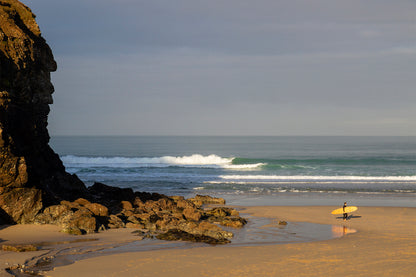 整った波が待つラインナップへ。中空構造（ホロー）の木製サーフボード（天然木）を抱え、長い影を落として歩く。職人の手仕事によるボードと共に自然の中へ帰っていく、上質な時間を楽しむ後ろ姿。
