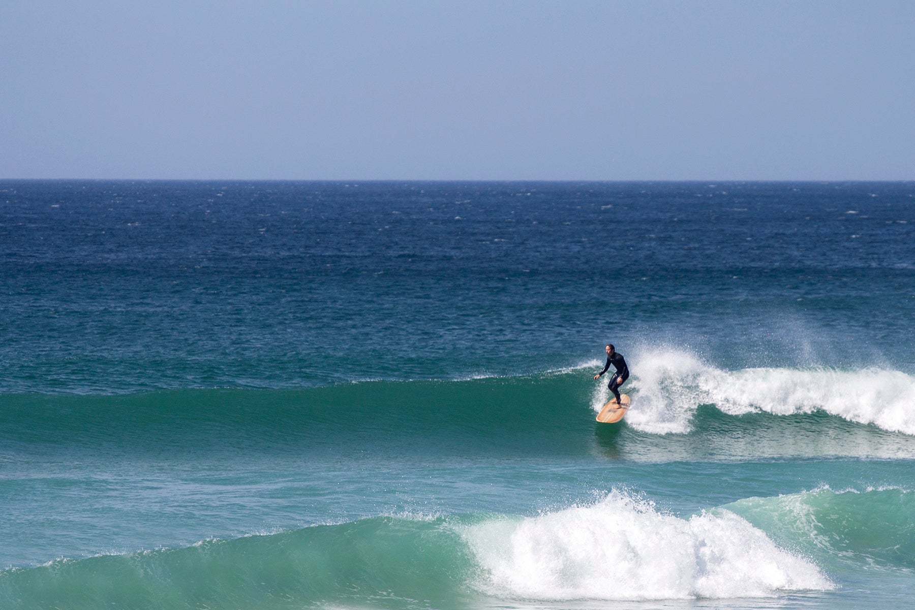 整ったフェイスを滑走する、中空構造（ホロー）の木製サーフボード（天然木）の安定感。職人の手仕事が生んだスムースな走り、大自然の中で信頼に応える上質なウッドのクオリティ。