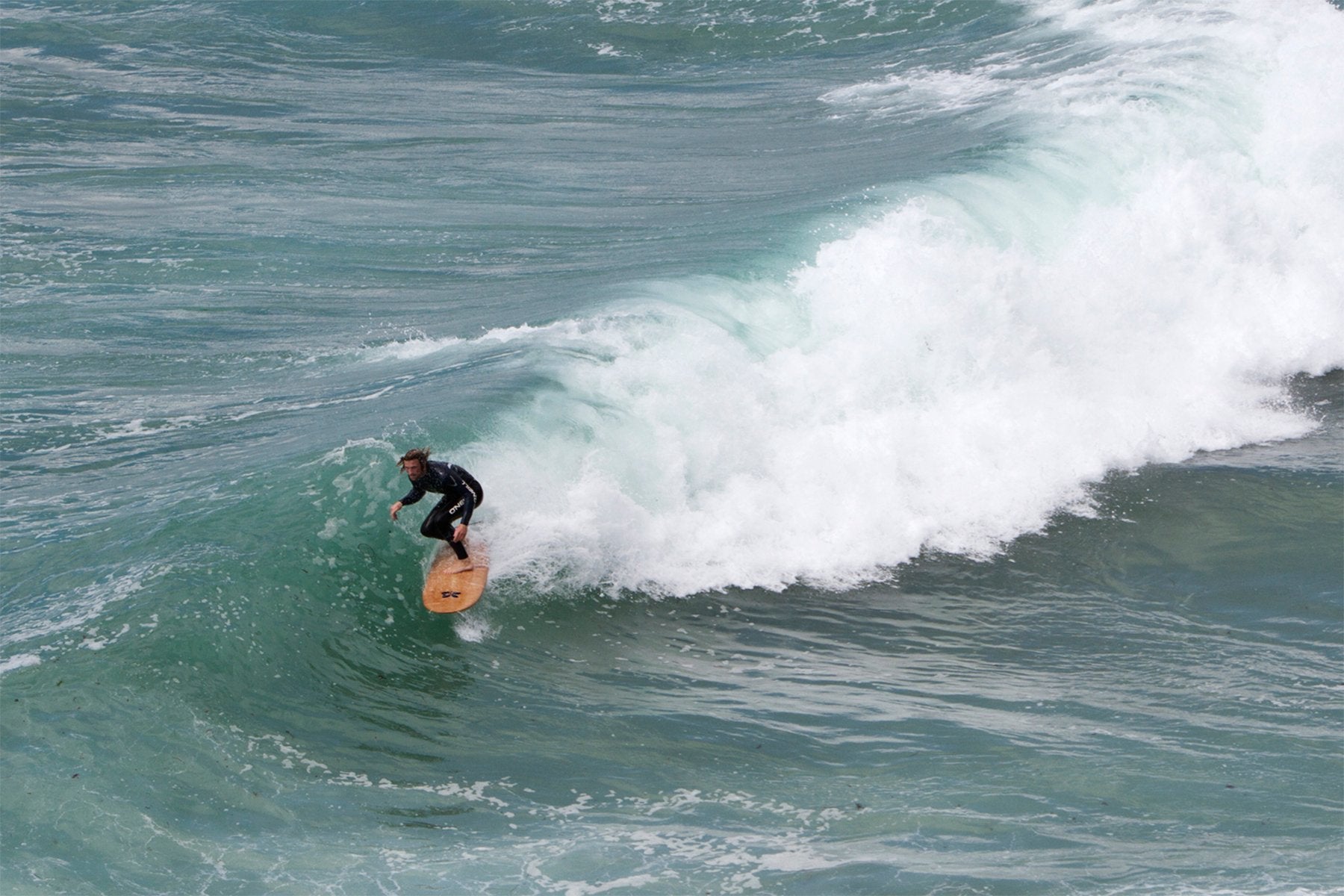 白波（スープ）が渦巻くセクションを抜けようとするサーファーと、中空構造（ホロー）の木製サーフボード（天然木）。俯瞰で捉えた構図が、荒れた水面でも安定感を失わないボードの優れた設計と洗練されたエコラグジュアリーな機能美を証明する。