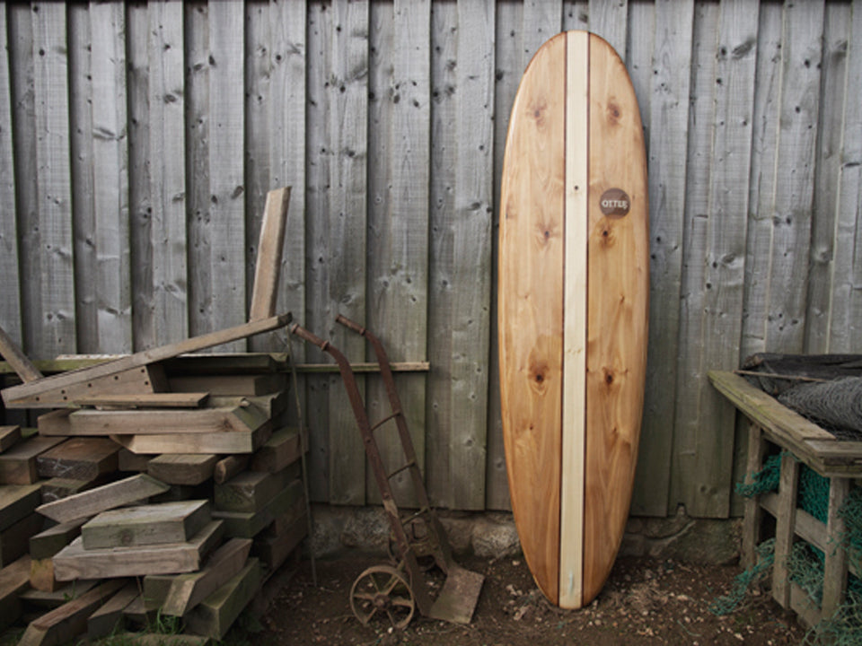 中空構造（ホロー）の木製サーフボード（天然木）の節のある木目と古材の背景。新旧のウッド素材が織りなす味わい深いコントラスト、飾れる・乗れるサステナブルな機能美。