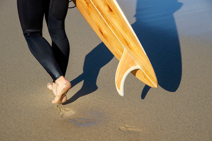 波乗りを終えた充実感か、これからの期待か。中空構造（ホロー）の木製サーフボード（天然木）を抱えて歩くビーチサイド。大地と繋がり、自然のリズムを感じる大人のサーフスタイル。