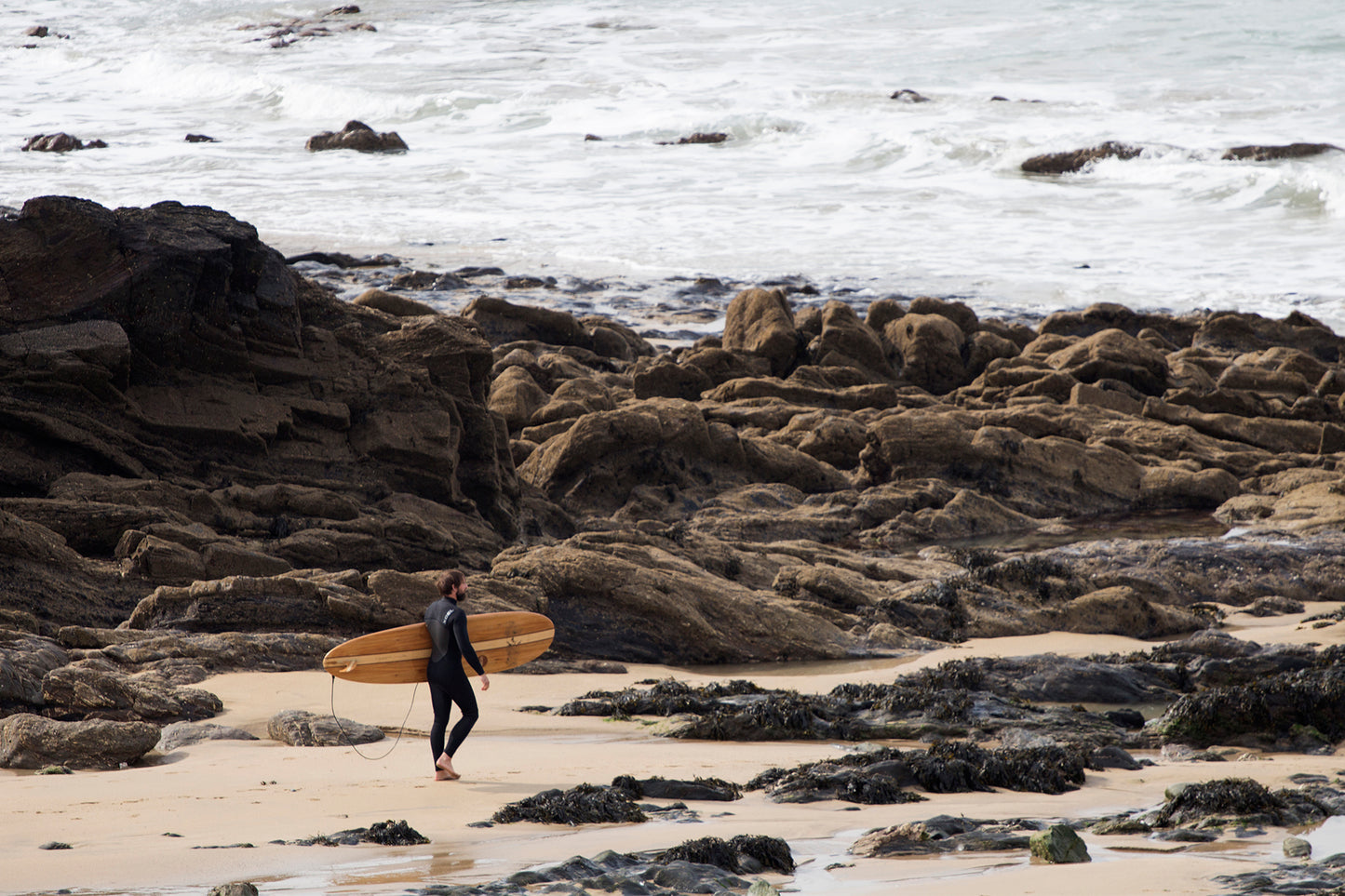 人の気配がない岩場のビーチ、理想のブレイクを求めて歩く。中空構造（ホロー）の木製サーフボード（天然木）と共に自然の奥深くへ踏み入る、静かで贅沢な大人のサーフタイム。