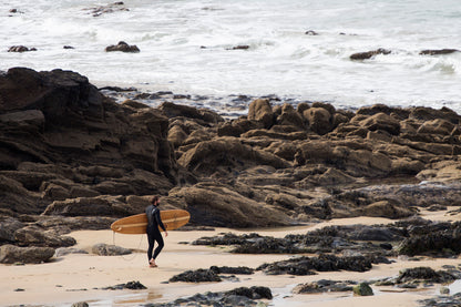 人の気配がない岩場のビーチ、理想のブレイクを求めて歩く。中空構造（ホロー）の木製サーフボード（天然木）と共に自然の奥深くへ踏み入る、静かで贅沢な大人のサーフタイム。